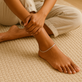 Woman sitting on a rug indoors, wearing a white tank top and light-colored pants and snake anklet