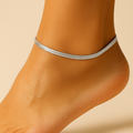Silver anklet on a person's ankle against a beige background